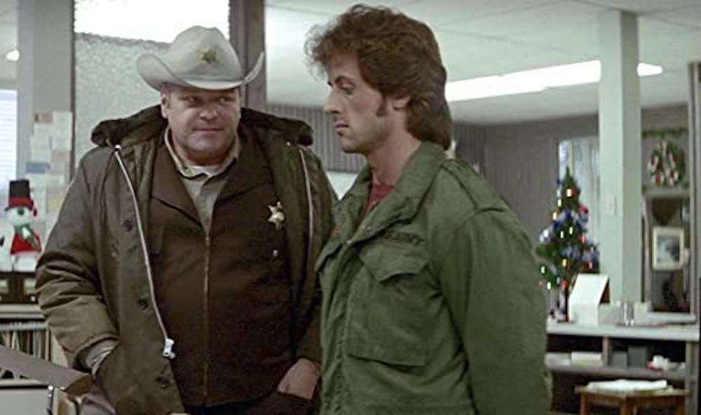 Still from First Blood: the sheriff and Rambo in a station with a Christmas tree behind them