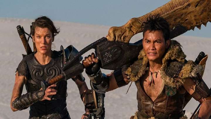Still from Monster Hunter: two hunters in armor carry huge weapons across a desert