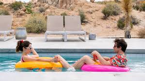 Still from Palm Springs: a man and a woman lounge on pool floats in a desert resort pool