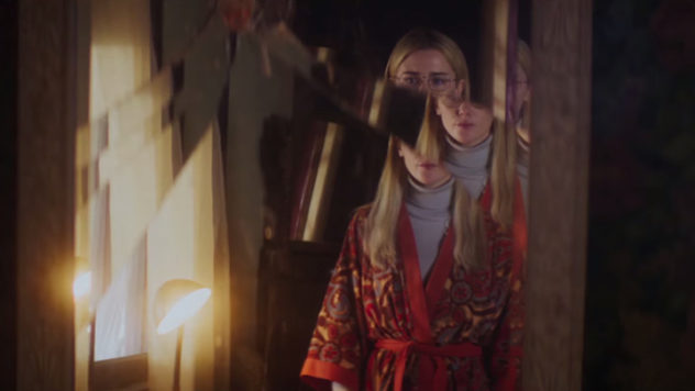 Still from When I'm A Moth: a blonde woman in a red patterned robe in a dim room