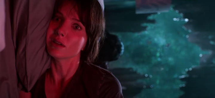 Still from Malignant: a frightened woman bathed in red light presses against a wall