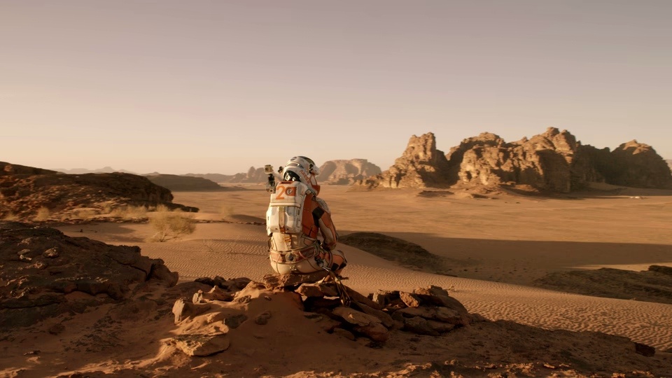 Still from The Martian: an astronaut in a spacesuit sits alone on a red Martian landscape