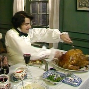 Still from Blackadder's Christmas Carol: Ebenezer Blackadder carves a roast turkey at a laden dinner table
