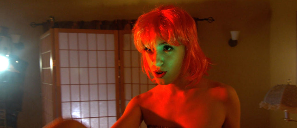 Still from Dreaming Hollywood: a woman in a red wig lit by red light
