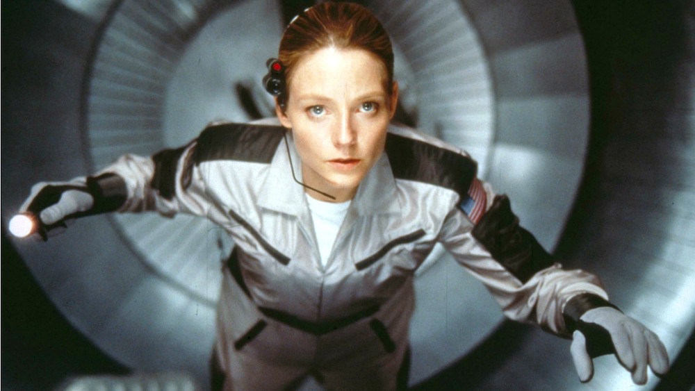 Still from Contact: Ellie in a flight suit, holding a flashlight, inside a circular metal pod