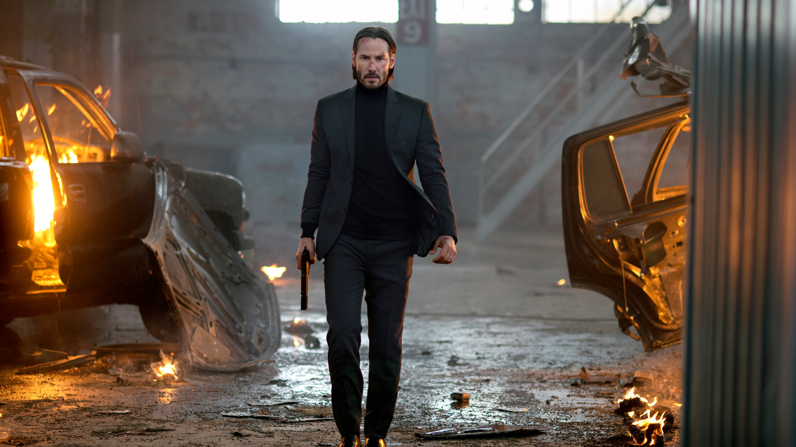 Still from John Wick: John walks past burning wrecked cars with a gun