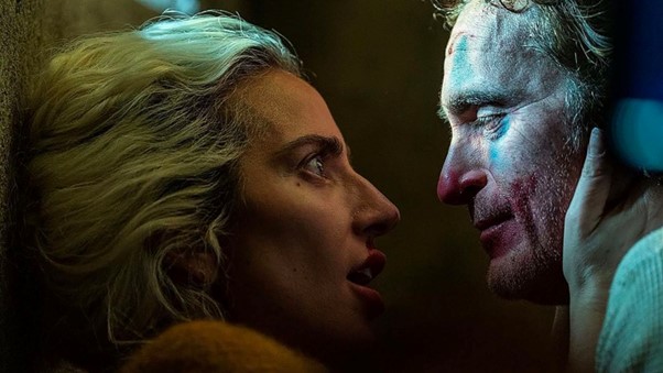 Still from Joker: Folie à Deux: Harley Quinn cradles the face of Joaquin Phoenix's Arthur Fleck in clown makeup