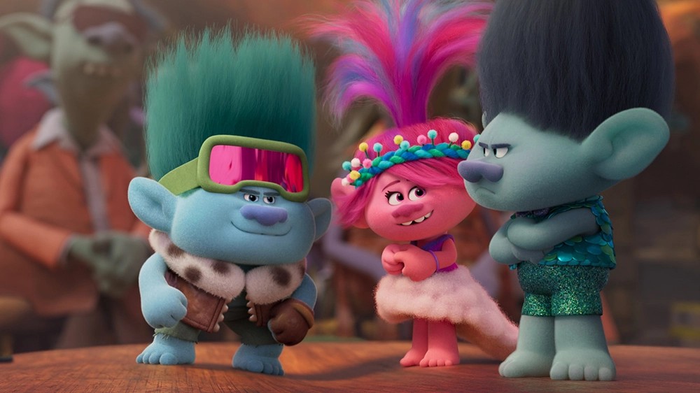 Still from Trolls Band Together: Poppy stands between two blue Trolls, one wearing goggles