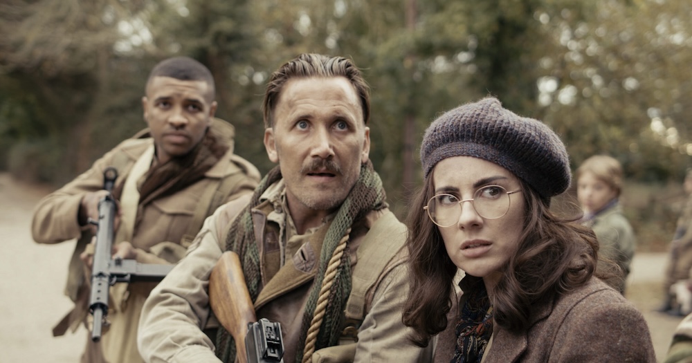 Still from Fortunes of War: armed soldiers and a woman in a beret look up warily in a wood