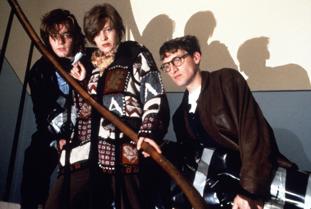 Still from Shallow Grave: the three flatmates lean on a staircase railing, their shadows on the wall behind