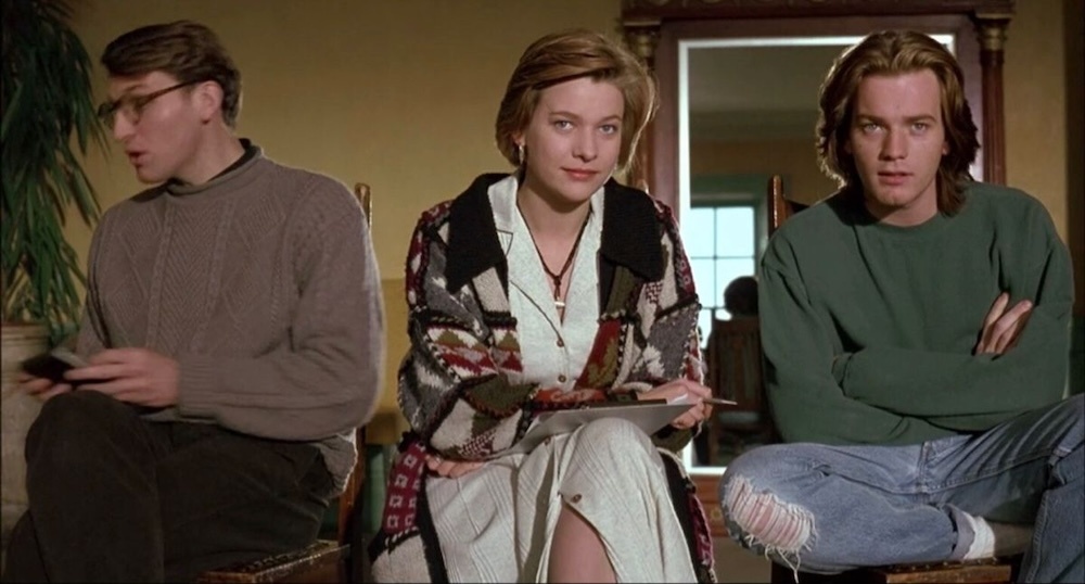Still from Shallow Grave: three flatmates sit in a row, the woman in the middle holding a clipboard