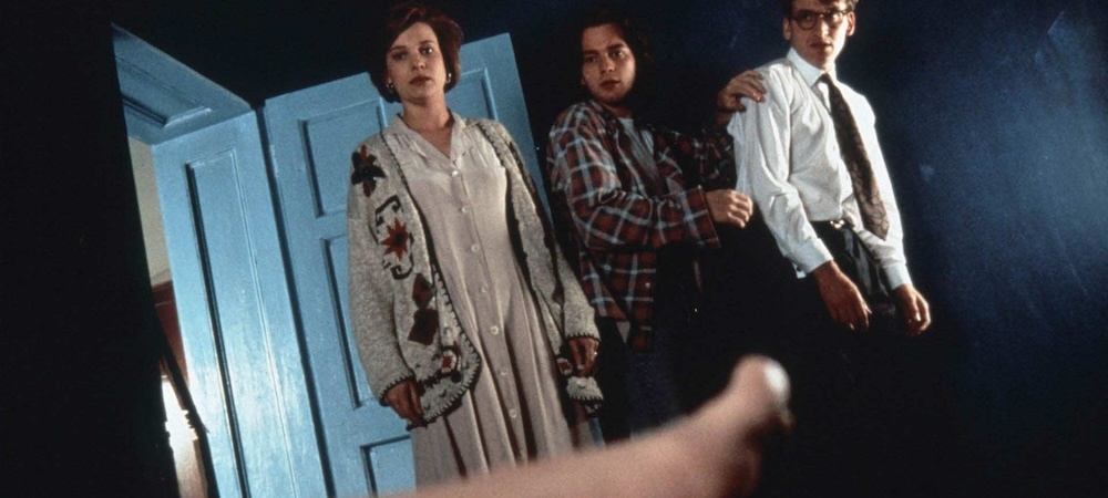 Still from Shallow Grave: three flatmates stand in a doorway looking at a body's outstretched arm