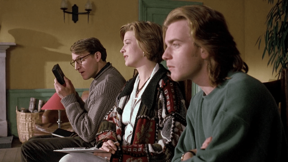 Still from Shallow Grave: the three flatmates sit side by side, one holding a phone
