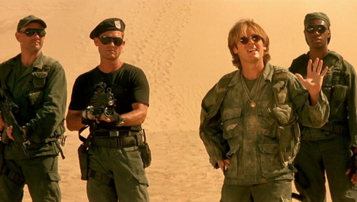 Still from Stargate: four soldiers in fatigues and a scientist waving in the desert