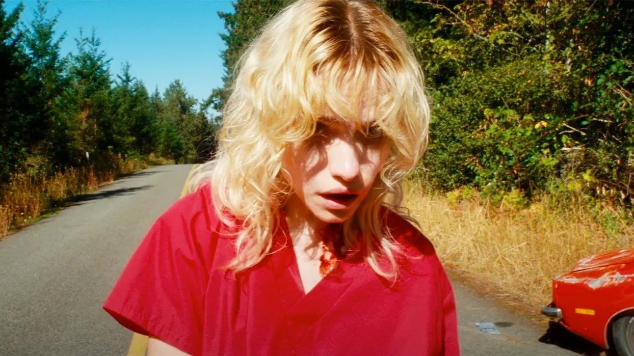 Still from Strange Darling: a startled blonde woman in a red shirt on a sunlit country road