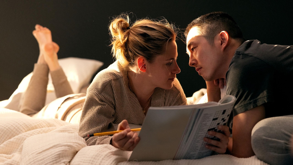 Still from Love Me: a couple lie on a bed working on a puzzle book together