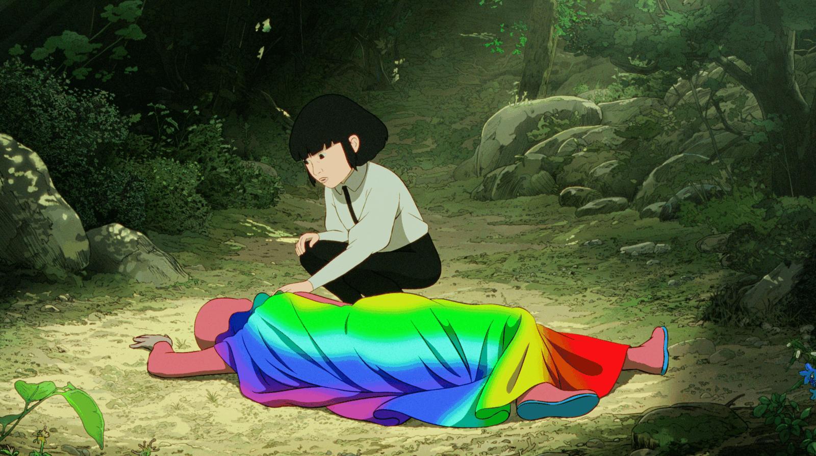 Still from Arco: a dark-haired girl kneels in a forest clearing beside a figure lying under a rainbow-striped cloak