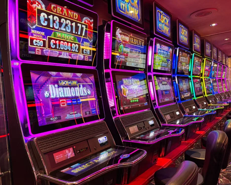 A long row of brightly lit slot machines glowing pink and purple in a casino